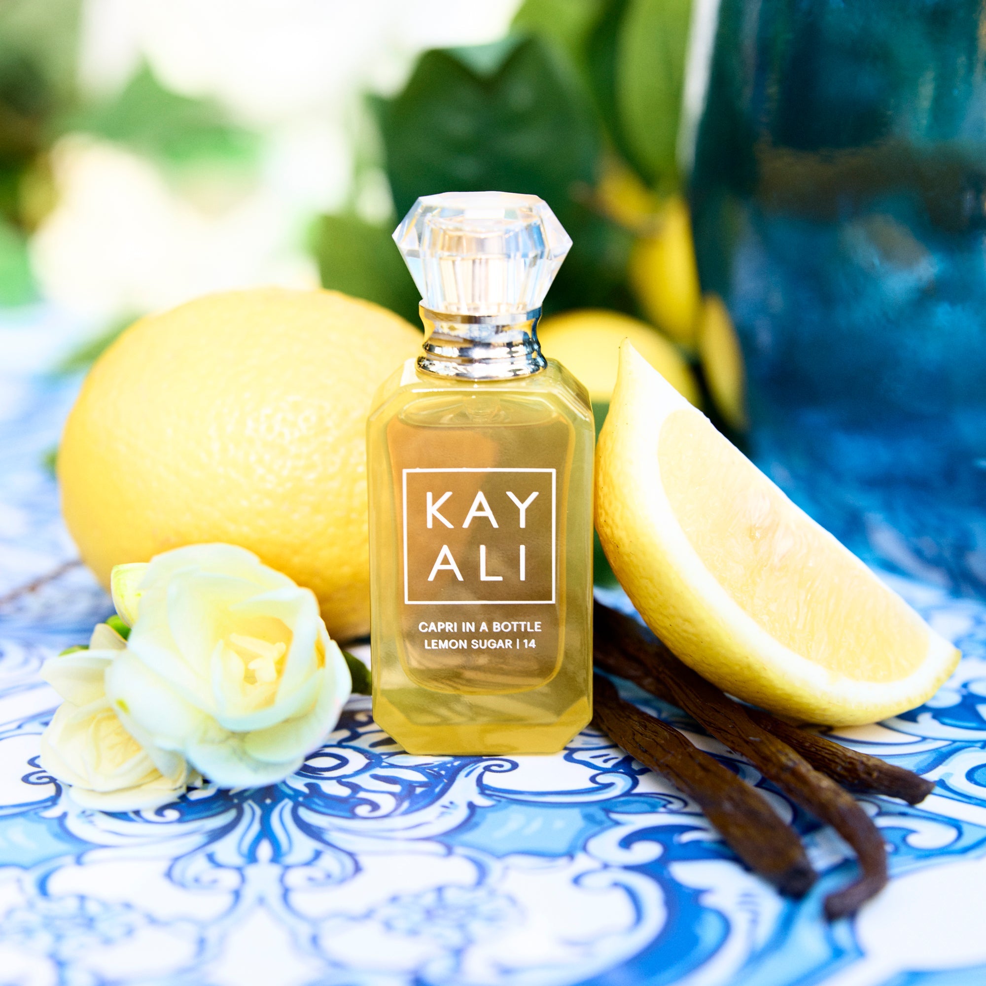 Bottle of KAYALI perfume with lemons, vanilla beans, and a rose on a decorative plate.
